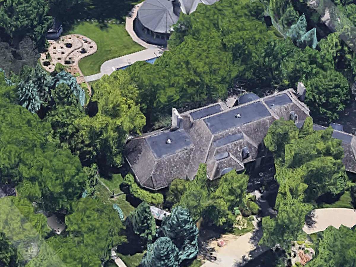 A large house surrounded by lush trees, with a circular building nearby and a winding path leading through a well-manicured lawn and garden area.