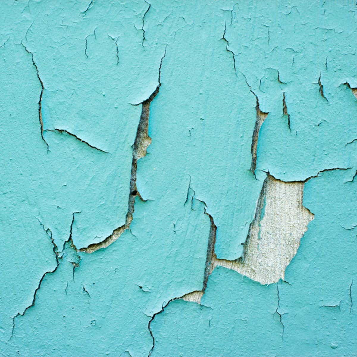 A textured turquoise wall displays peeling paint, revealing a lighter surface underneath, highlighting the passage of time and weathering effects.