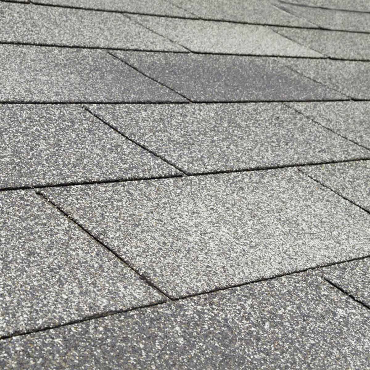 Gray asphalt shingles cover a sloped roof, arranged in a staggered pattern, showcasing a textured surface that glints softly in the light.