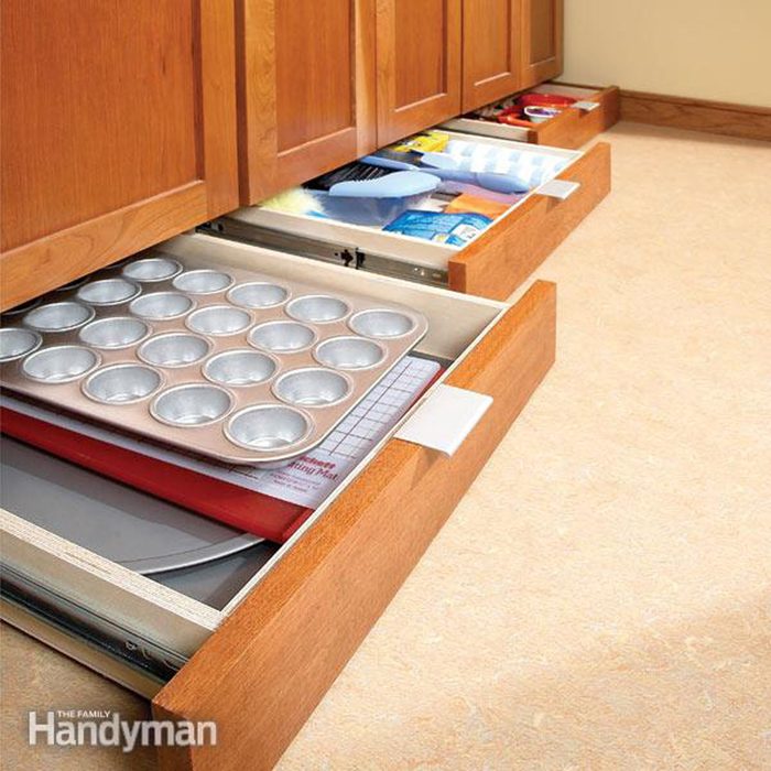 Drawers under a wooden kitchen cabinet hold baking trays and utensils, showcasing organized kitchen tools against a light-colored floor.