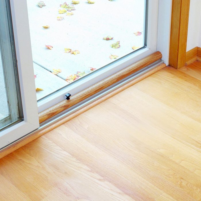 A sliding glass door opens to a patio with scattered autumn leaves, revealing a smooth wood floor and a clean, indoor environment.
