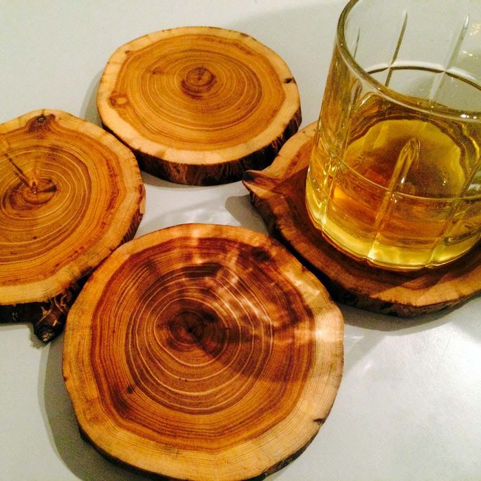A glass of yellow liquid rests on a wooden coaster among three other circular wood coasters, set against a light-colored surface.