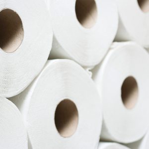 White toilet paper rolls are stacked closely together, showcasing their cylindrical shape and cardboard cores. The setting appears to be a storage area.