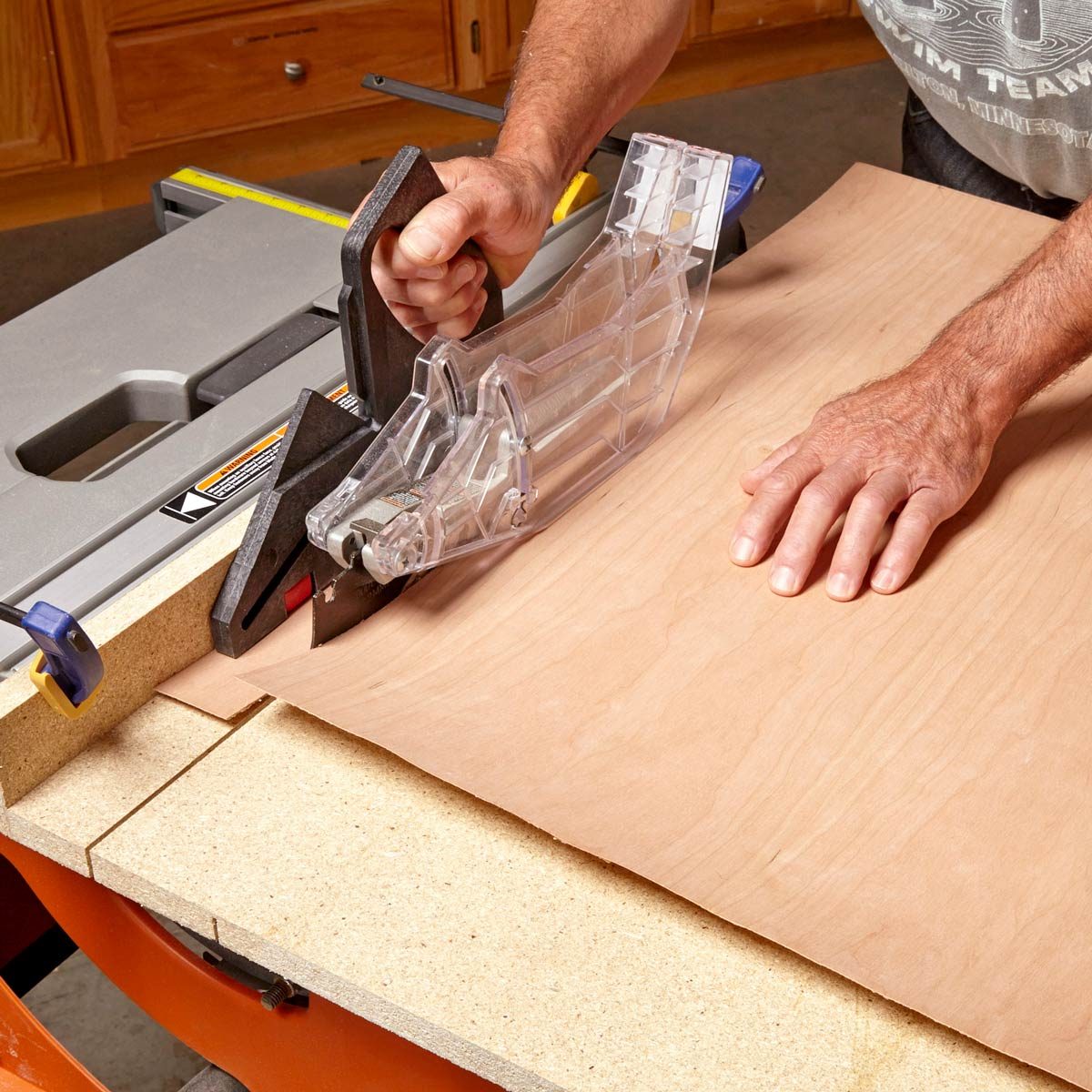 A person uses a handheld tool to guide a cutting blade across a piece of wood on a workbench, surrounded by workshop equipment.