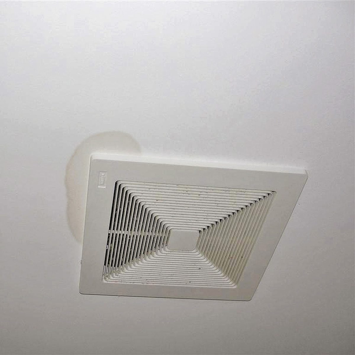 A ceiling vent is mounted, releasing air, with a water stain on the white ceiling nearby, indicating potential moisture issues in the surrounding area.