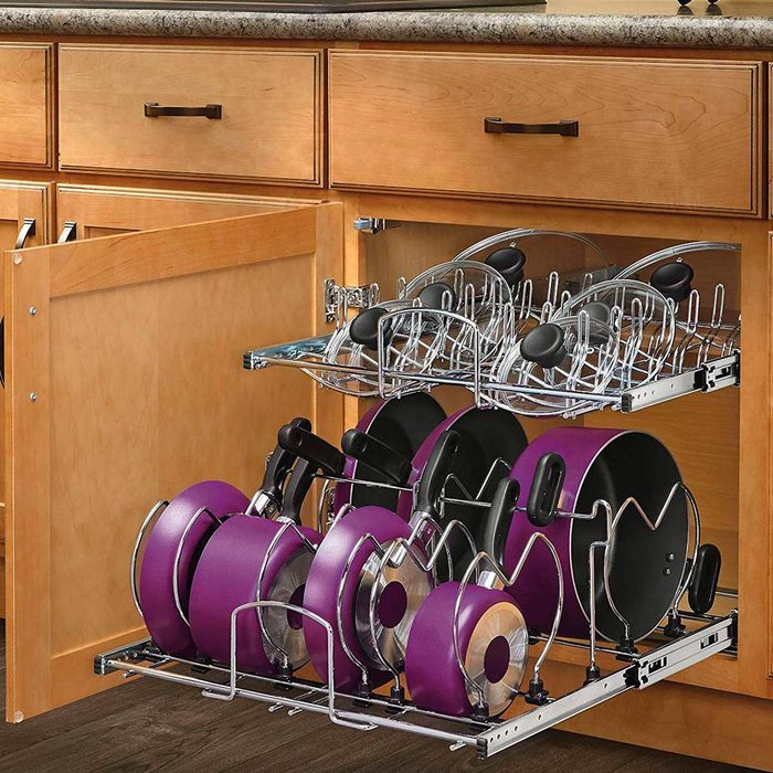 A pull-out kitchen cabinet organizes purple pots and lids on chrome racks, situated beneath a countertop with wooden cabinets above.