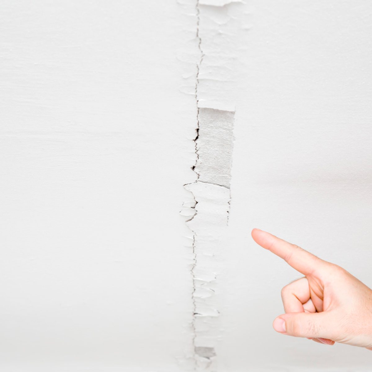 A hand points at a cracked ceiling, highlighting the irregular break in the smooth white surface above, indicating potential damage or disrepair.