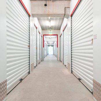 A hallway lined with metallic storage unit doors is illuminated by overhead lights, leading to an exit at the far end.