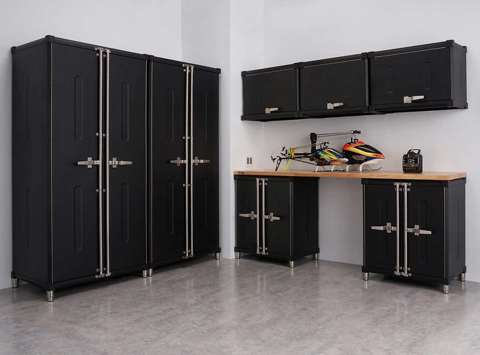Black storage cabinets stand neatly against a gray wall, while a workbench displays remote-controlled helicopters and equipment in a clean, organized space.