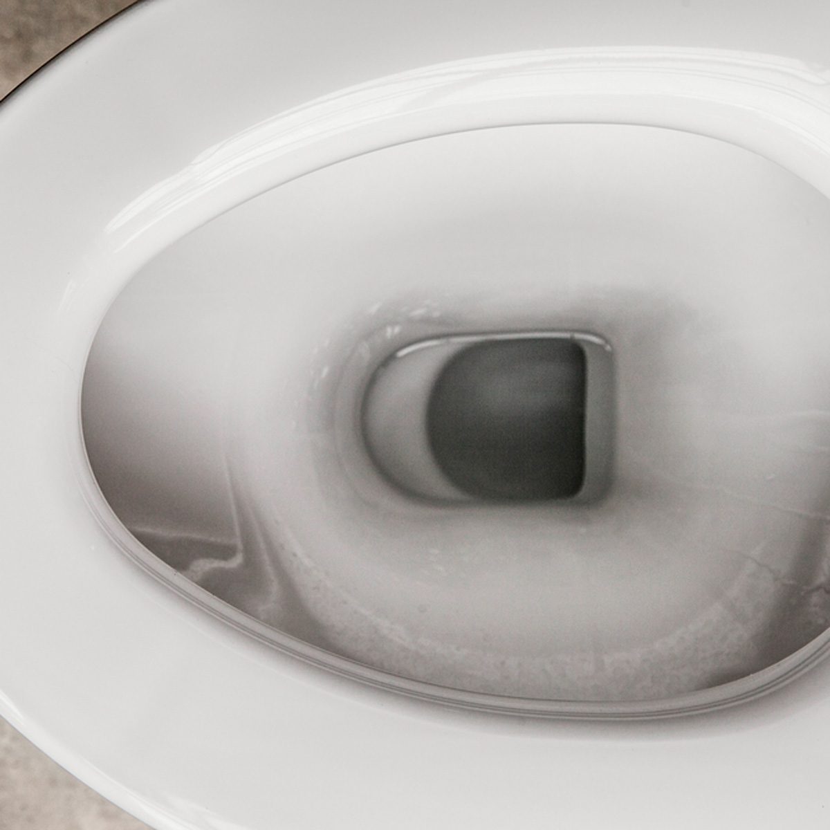 A toilet bowl is visible, with water reflecting a dark shape in the center. The setting appears neutral and minimalistic, possibly a bathroom environment.