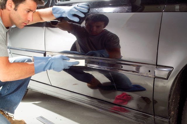 a person scraping the old adhesive from a car window with a plastic putty knife