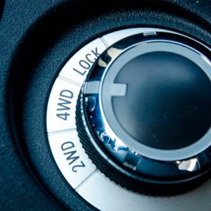 A shiny control dial is being adjusted. It features settings for 2WD, 4WD, and LOCK, mounted on a textured black surface, likely in a vehicle.