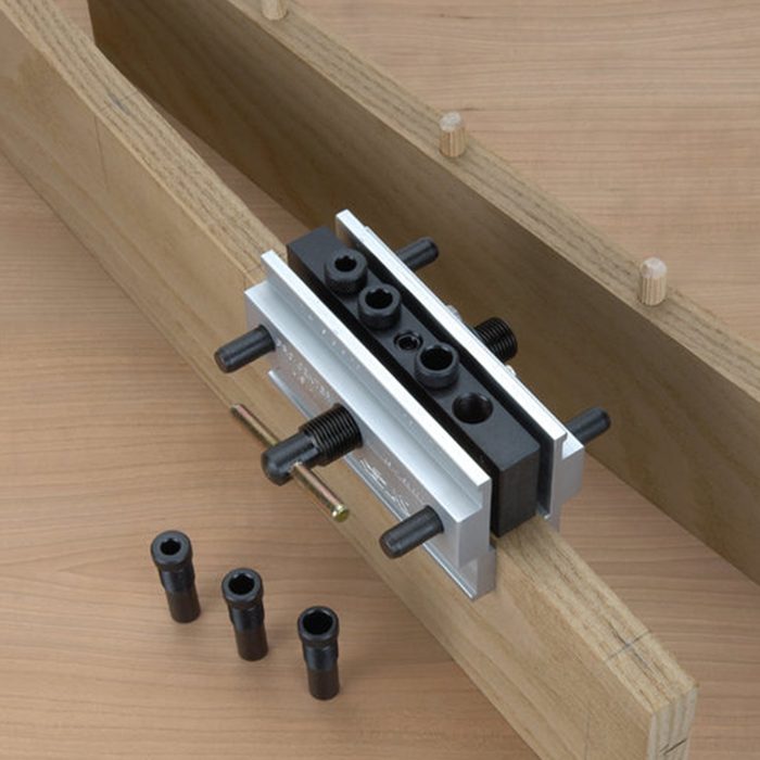 A clamping guide is positioned on a wooden beam, with three cylindrical connectors placed nearby, facilitating precise alignment and assembly.