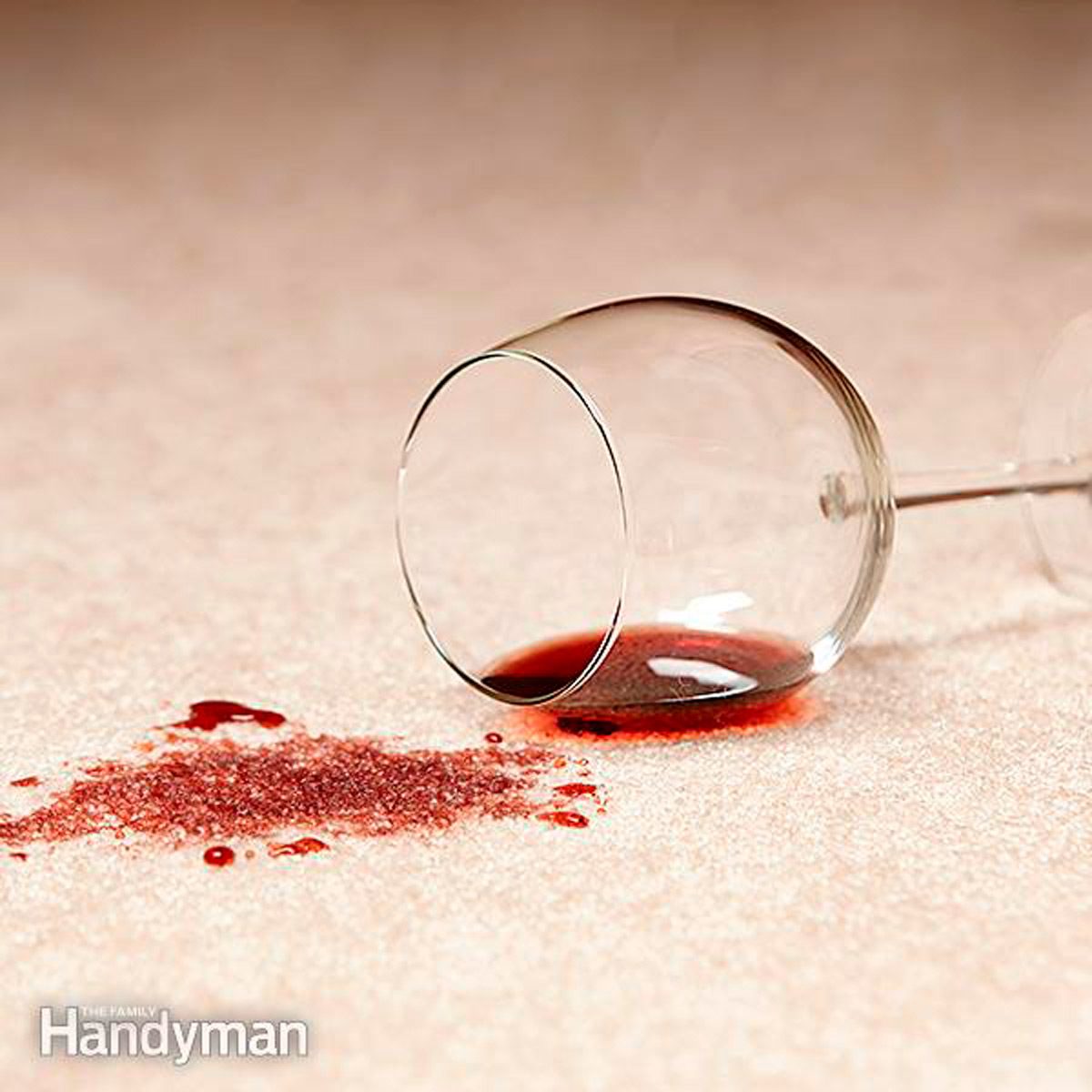 A tipped wine glass spills red liquid onto a light-colored carpet, creating stains and a mess in the surrounding area.