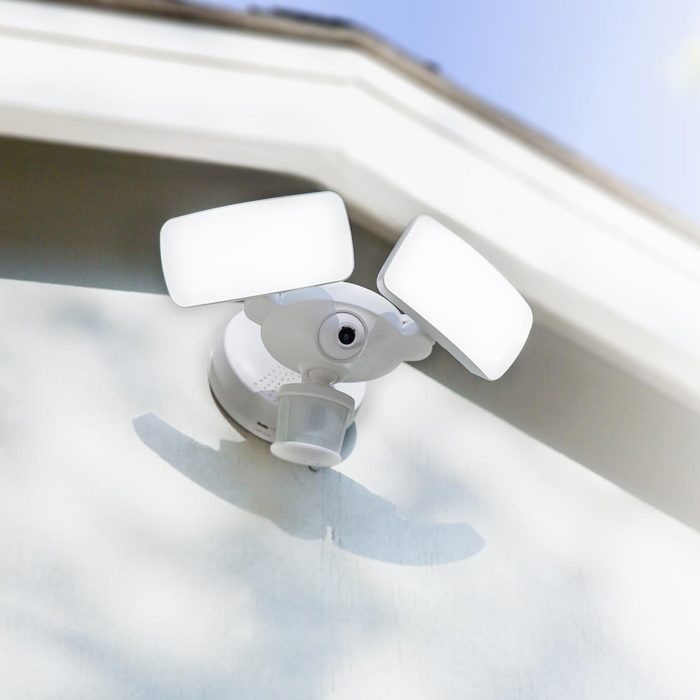 A motion-sensor security light is mounted on a wall, illuminating an area while detecting movement in an outdoor, sunny environment.