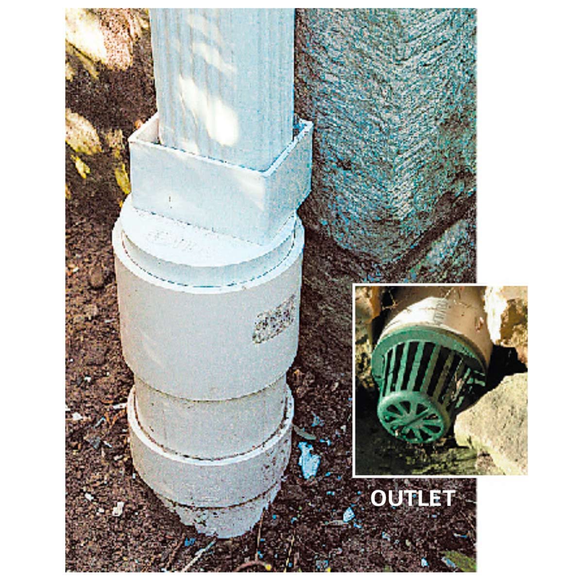 A white drainage pipe links to a green outlet, situated near a rocky surface in a dirt area, facilitating water flow away from the structure.