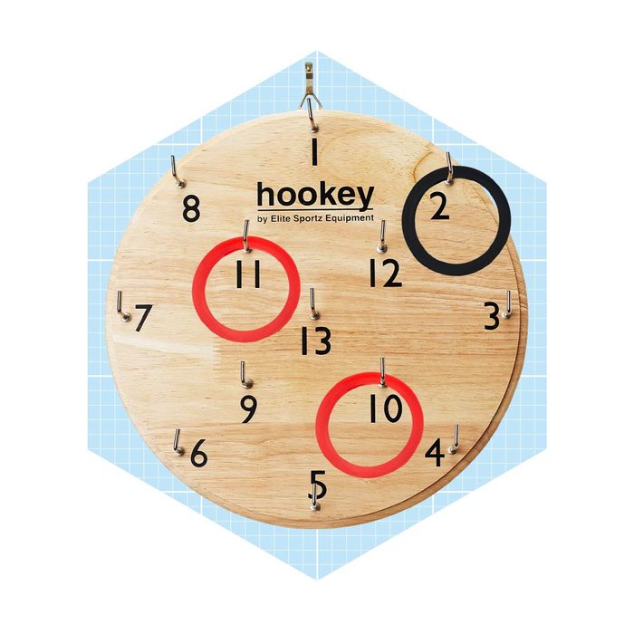 A circular wooden board displays numbered hooks and colored rings, indicating where game pieces can be placed. The background features a light blue grid pattern.