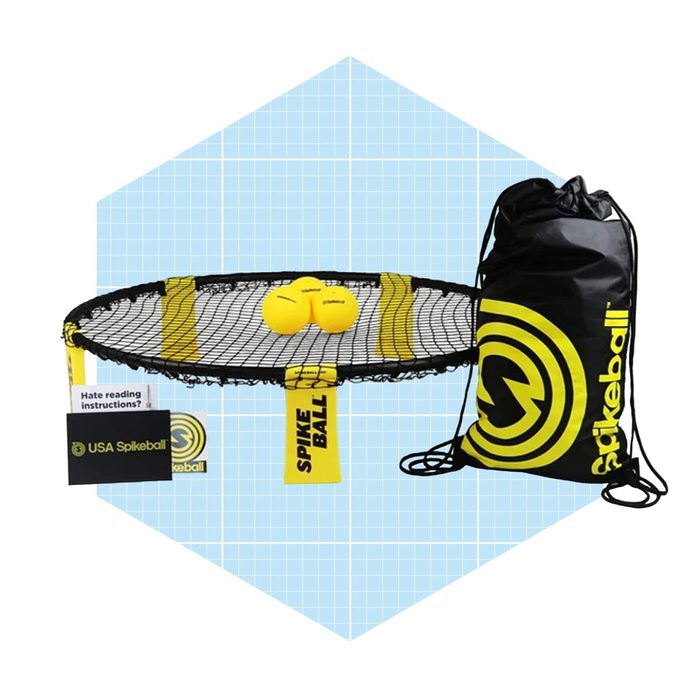 A spikeball net with two yellow balls rests on a blue, grid-patterned background, accompanied by a black drawstring bag and instructions.