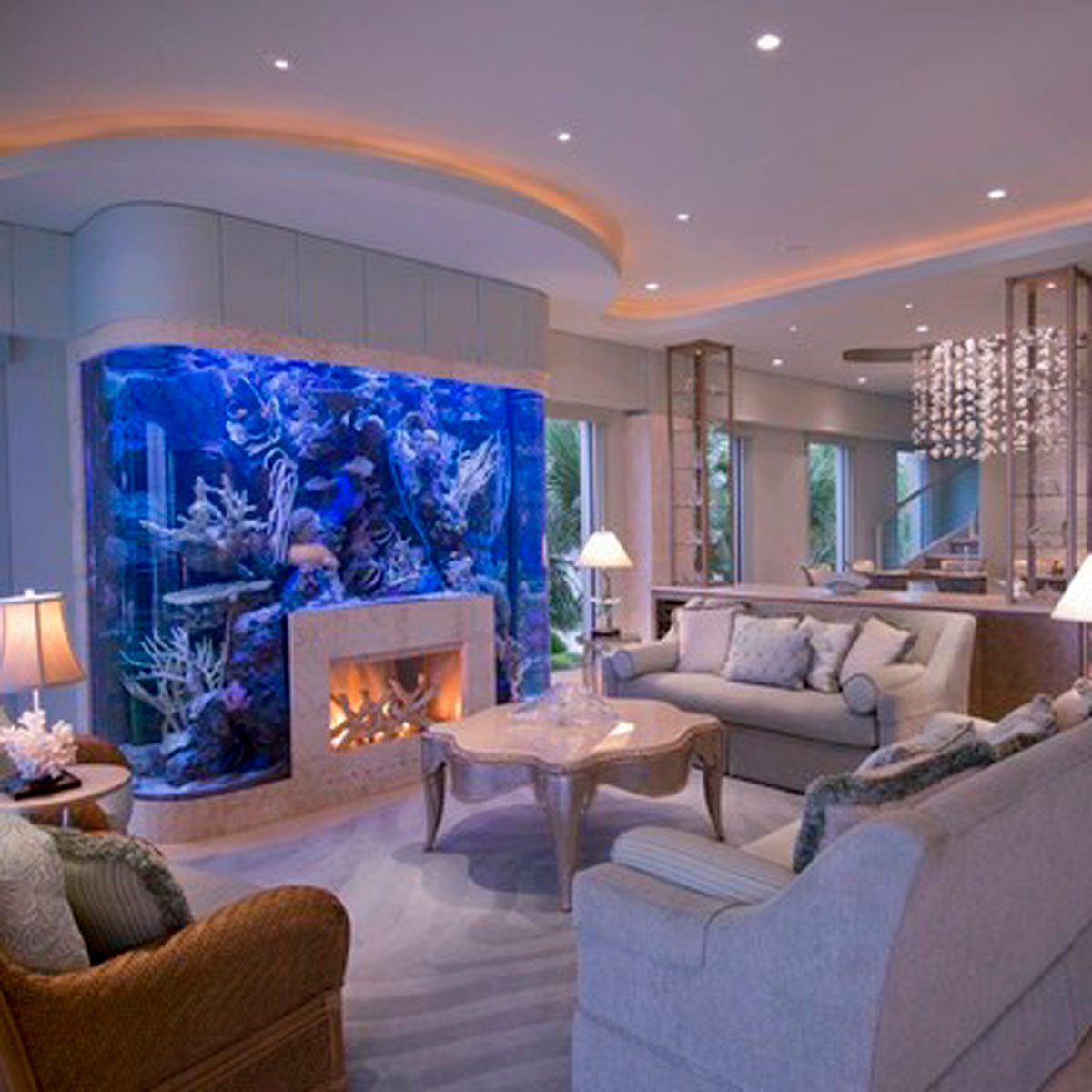 A large, colorful aquarium features marine life, positioned beside a modern fireplace in an elegant living room with soft lighting and tasteful furnishings.