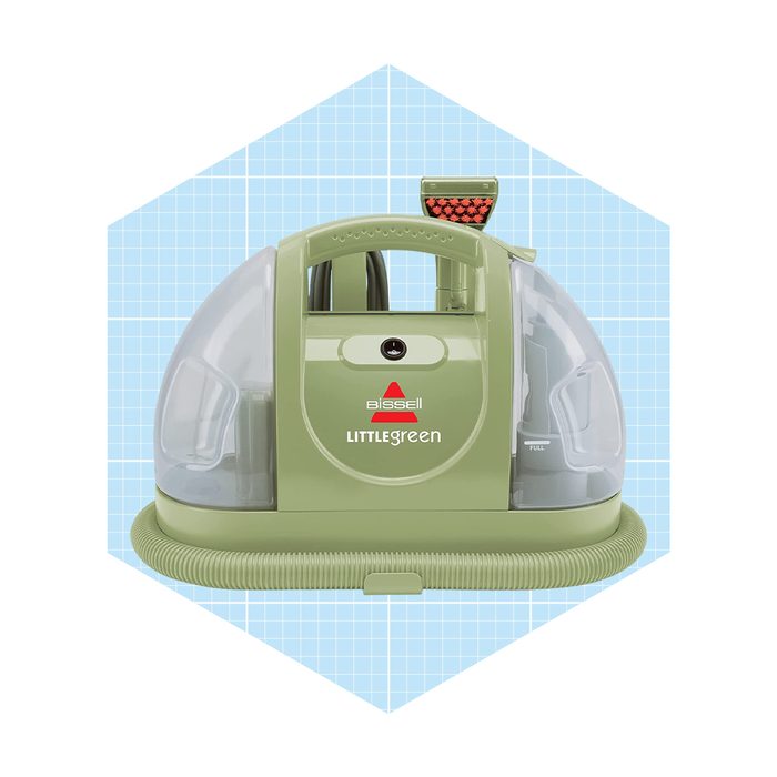 A compact, green carpet cleaner displays a clear tank, a handle, and a flexible hose, set against a light blue grid background.