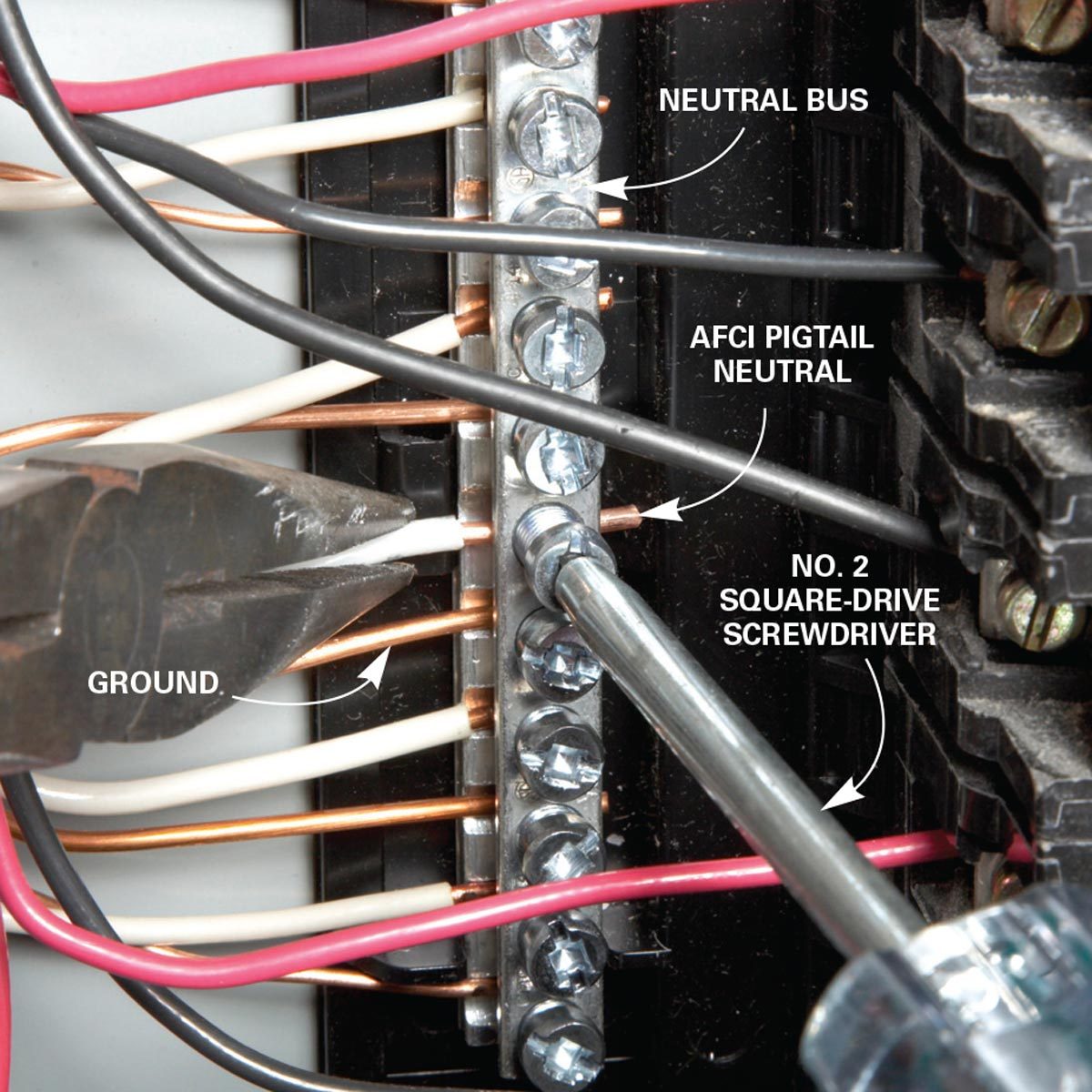 A screwdriver connects wires to a neutral bus in an electrical panel, surrounded by various colored wires and pliers, indicating tools for electrical work.