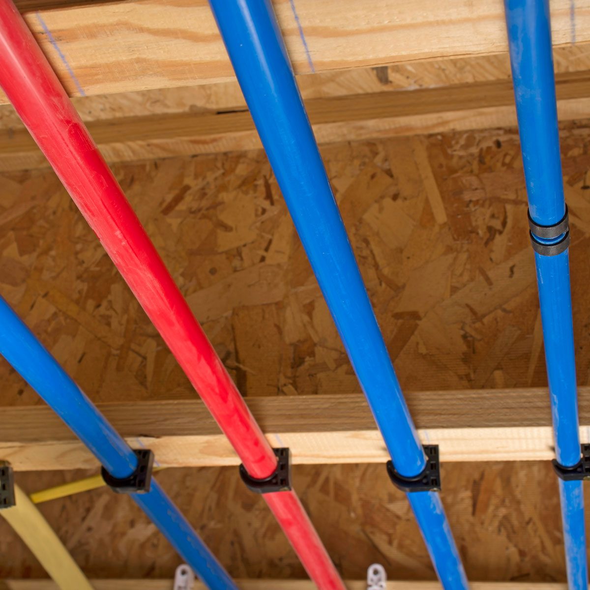 Colored pipes (red and blue) are installed horizontally on a wooden framework above a textured surface. The setting appears to be a construction or plumbing area.