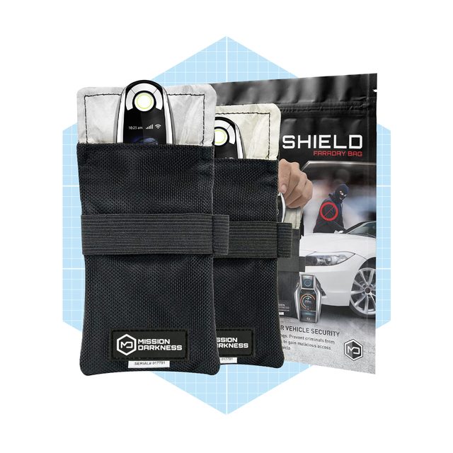 Two black Faraday bags hold car key fobs designed to block signals, placed against a backdrop featuring a vehicle security advertisement.
