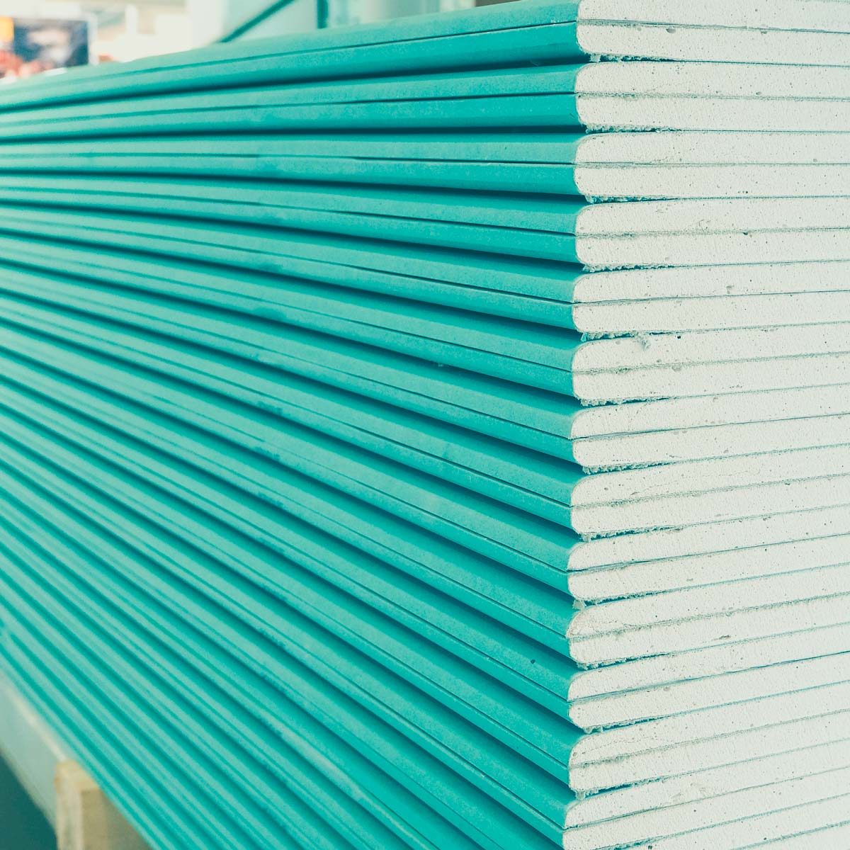 Stacks of green-tinted drywall panels are aligned horizontally, with their edges visible. They are placed in a construction setting, suggesting preparation for building.