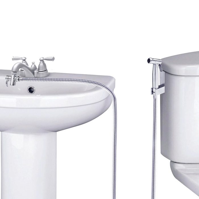 A white sink with silver faucets sits next to a toilet, connected by a flexible hose, suggesting a plumbing fixture in a bathroom setting.