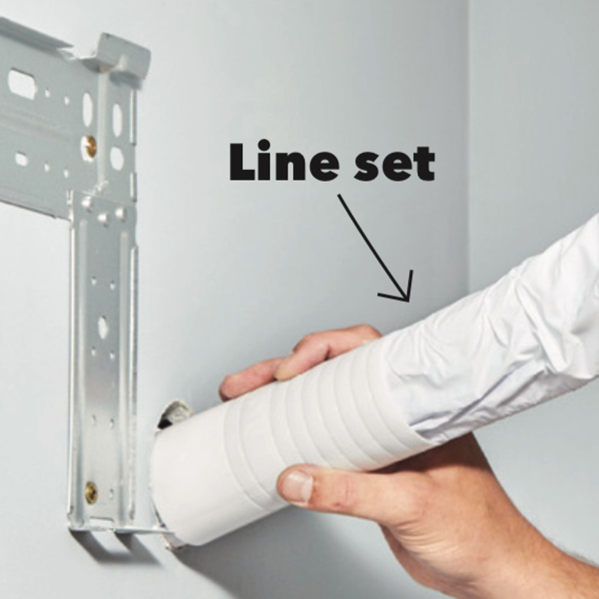A person is inserting a white line set into a wall mount in a room with light-colored walls, indicating installation or repair work.