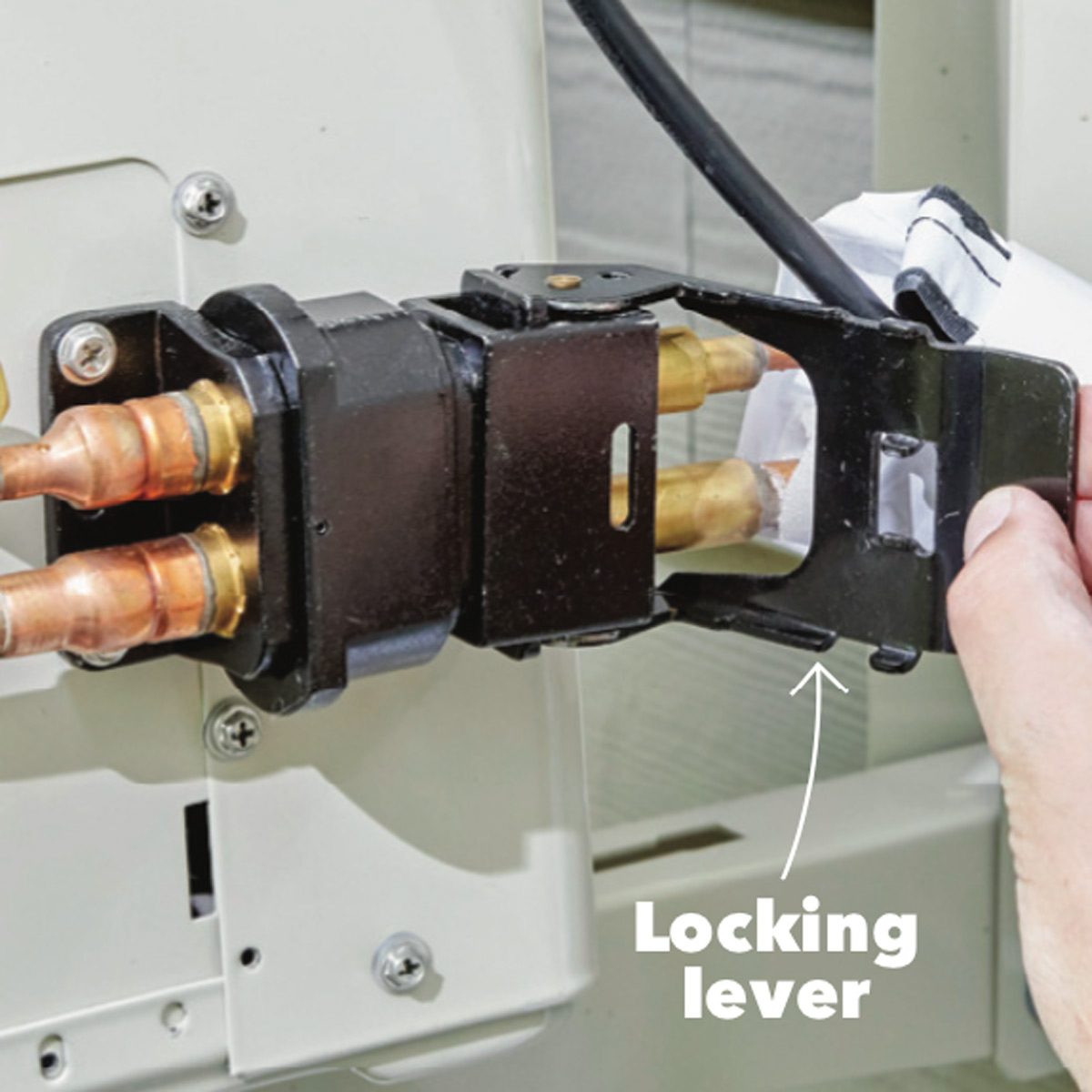 A hand holds a locking lever connected to a metal component with copper pipes, positioned against a light backdrop, indicating a mechanical adjustment process.