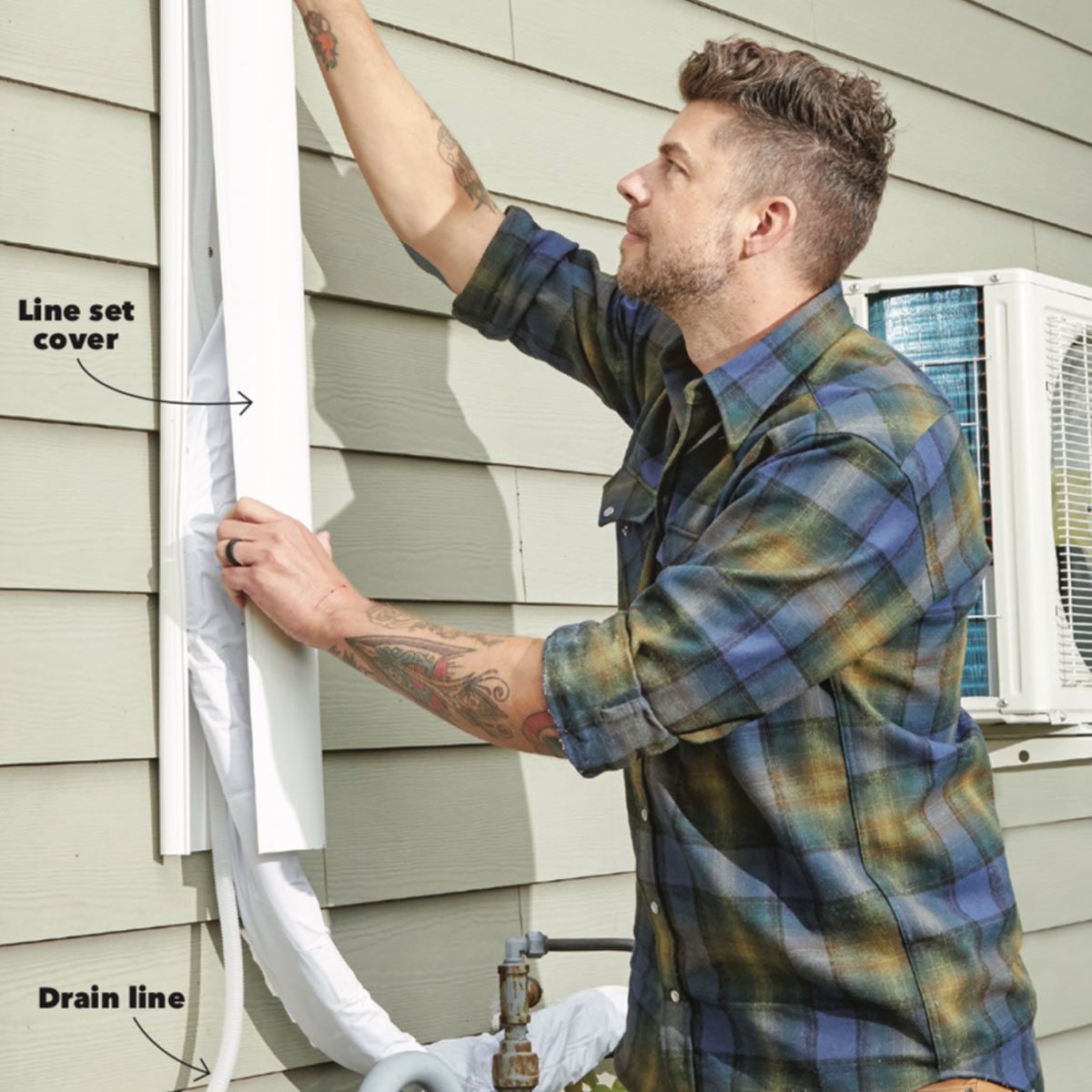 A man installs a line set cover on an exterior wall next to an air conditioning unit, handling the drain line below.