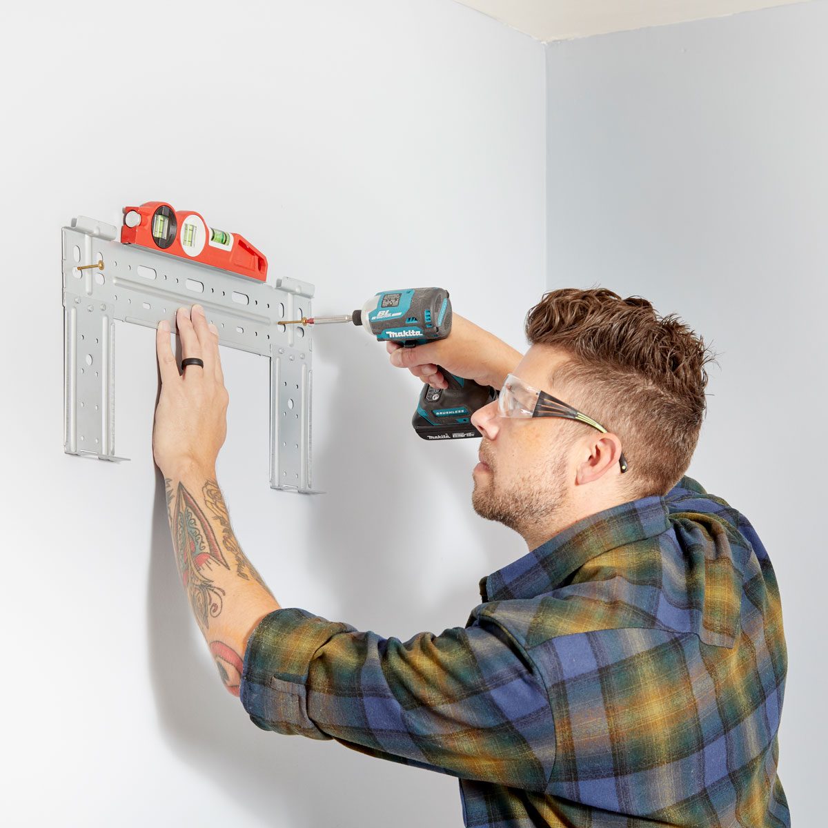 A person installs a metal bracket on a wall using a power drill, while a level rests on top, ensuring it is straight.