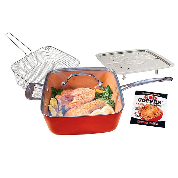 A copper square pan holds seasoned salmon with herbs and lemon, accompanied by a wire basket, a perforated lid, and a recipe guide.