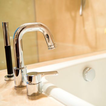 A chrome faucet is positioned above a bathtub, with water possibly flowing. The background features light-colored walls, creating a warm, inviting atmosphere.