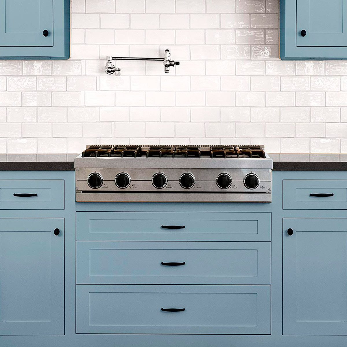 A stainless steel gas stove with five burners is set against a white tiled backsplash, surrounded by blue cabinets and a dark countertop.