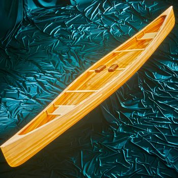 A wooden canoe rests on shimmering teal fabric, highlighting its smooth lines and design, suggesting a tranquil, water-related activity.
