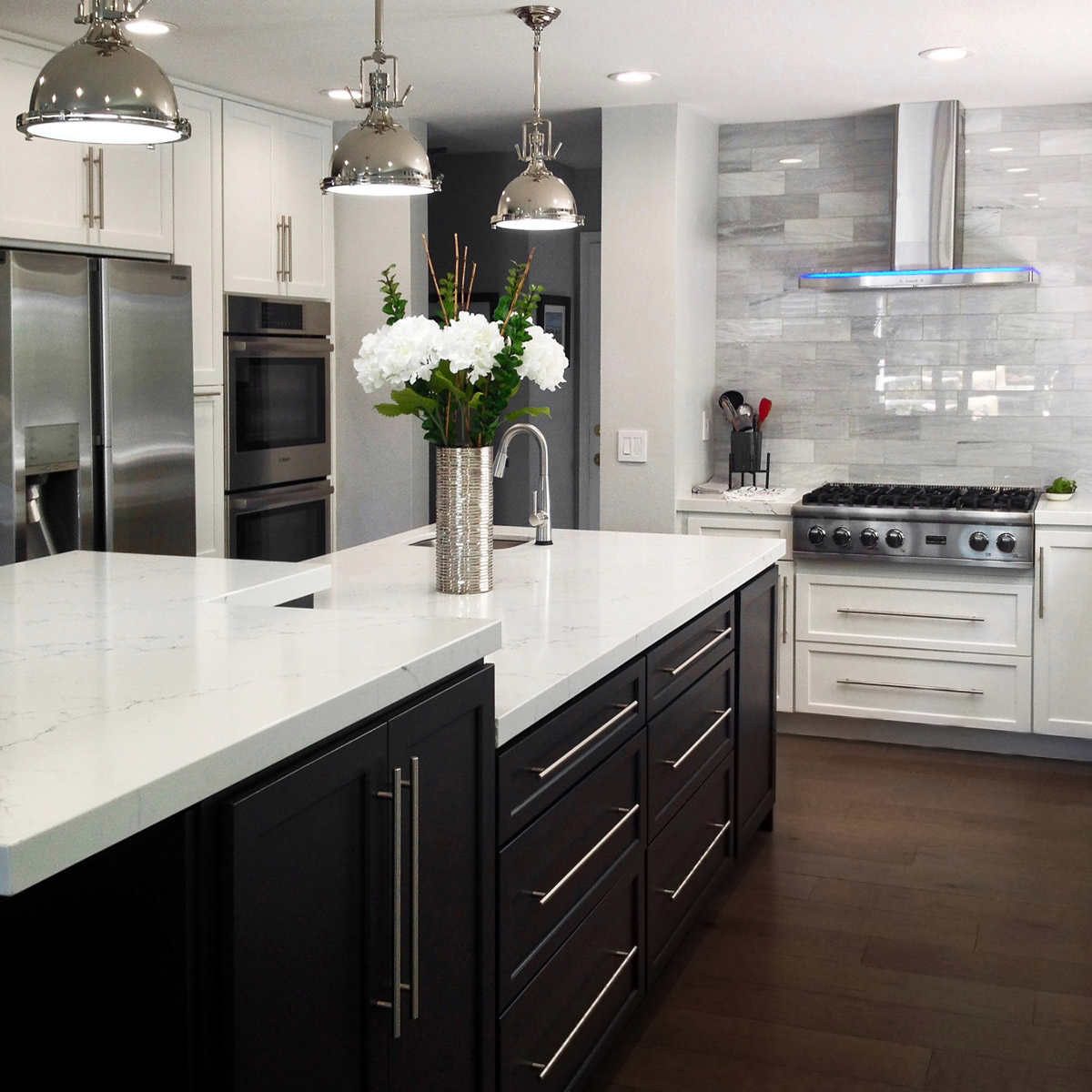 A modern kitchen features a sleek island with a flower vase, stainless steel appliances, and a gas stove, illuminated by stylish pendant lights.
