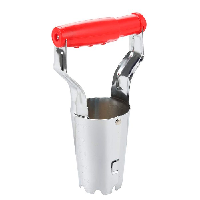 A metal soil auger with a red plastic handle is positioned upright, designed for digging into the ground effectively.