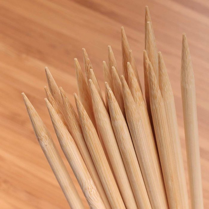 A bundle of pointed wooden skewers stands upright on a smooth surface, showcasing their sharp tips against a light wooden backdrop.