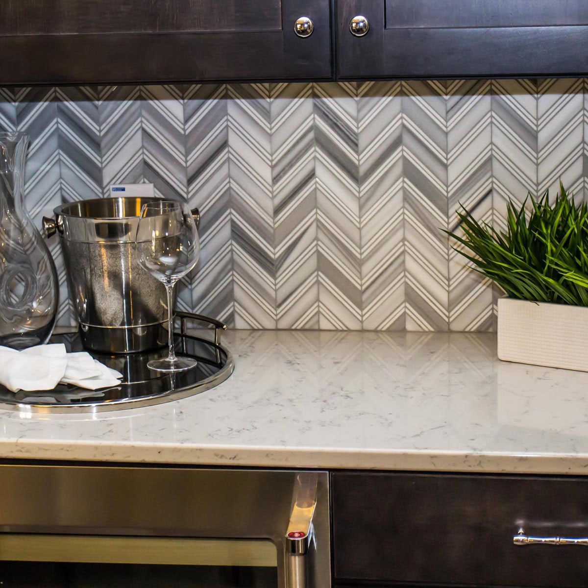 close up of white and grey chevron black splash with a light stone countertop and dark wood cabinets