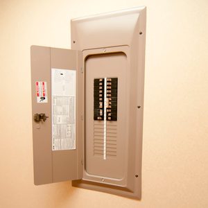 A beige electrical panel is open, displaying multiple circuit breakers inside. It is mounted on a plain wall, revealing informative labels and instructions.