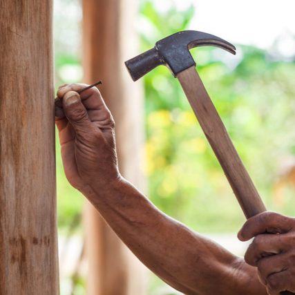 The carpenter is repairing the house. He makes nails using a hammer