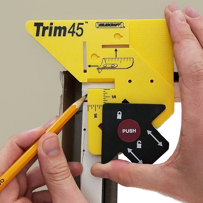 A hand holds a yellow trim tool against a surface, while a pencil marks a measurement, aiding precise cutting in a home improvement setting.