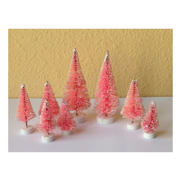 Small decorative pink trees stand upright on white bases against a textured yellow wall, arranged in varying heights and sizes.