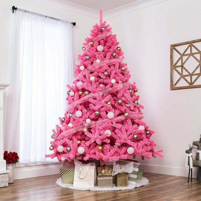 A vibrant pink Christmas tree adorned with ornaments stands in a brightly lit room, surrounded by wrapped gifts and a decorative wall piece.