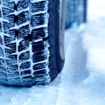 A tire with a detailed tread is resting on a snow-covered surface, displaying snow accumulation within the tread grooves.