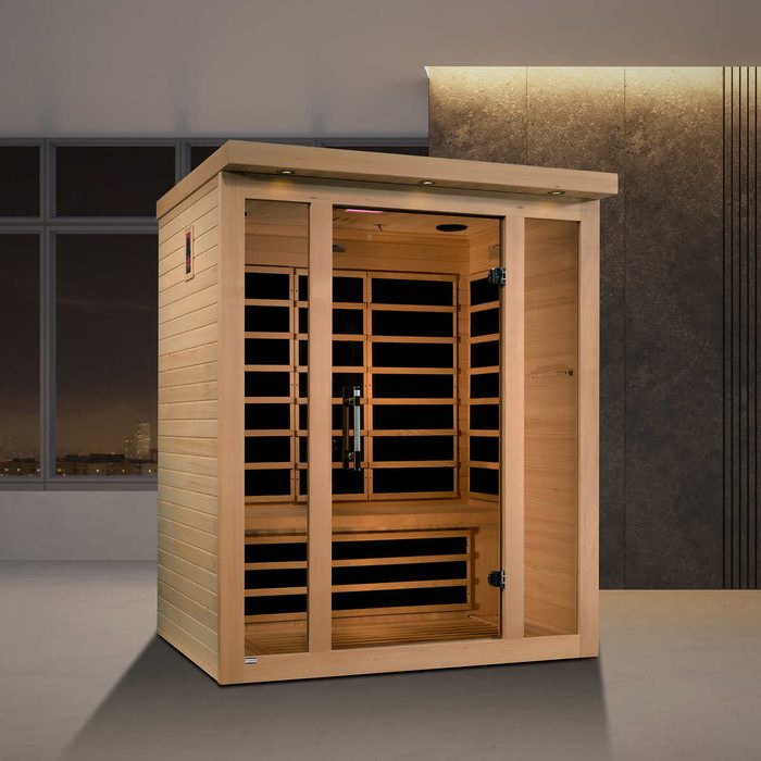 A wooden sauna stands upright in a modern room, featuring glass doors and wooden slats, providing a warm, relaxing space against a dark wall.