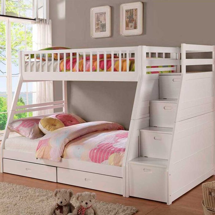 A white bunk bed with a lower bed and stairs features colorful bedding, set in a well-lit room with large windows and green views.