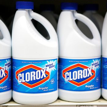 White plastic bottles of Clorox bleach are displayed on a store shelf, showcasing blue labels highlighting cleaning properties, with a consistent arrangement.